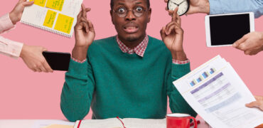 horizontal-shot-wishful-dark-skinned-man-crosses-fingers-makes-wish-dressed-green-sweater-prepares-examination-session-surrounded-with-alarm-clock-touchpad